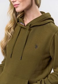Olijfgroene hoodie met een kangoeroezak, trekkoorden en een klein zwart logo. Heeft een subtiel gestreept accent bij de hals. Zacht materiaal.