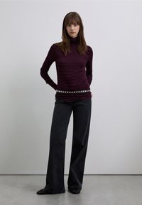 Long-sleeve turtleneck in dark purple with thin black stripes, paired with high-waisted wide-leg black jeans and a silver studded belt.