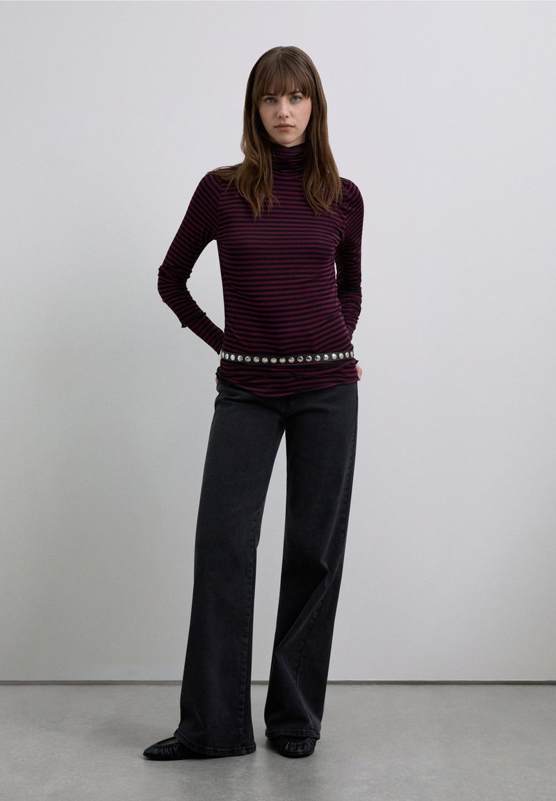 Long-sleeve turtleneck in dark purple with thin black stripes, paired with high-waisted wide-leg black jeans and a silver studded belt.