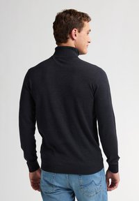 Czarny golf w ciemnoszarym kolorze z długimi rękawami, prążkowanymi mankietami i dołem, noszony z jasnoniebieskimi dżinsami, ukazujący gładką teksturę i dopasowany krój.