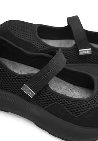 Zapatillas atléticas de malla negra con una superficie texturada, que presentan una correa ancha en el empeine y un detalle de marca en plateado.