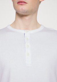 Maglietta henley lilla chiaro in tessuto morbido, caratterizzata da un collo rotondo, placca con cinque bottoni e una trama sottile.