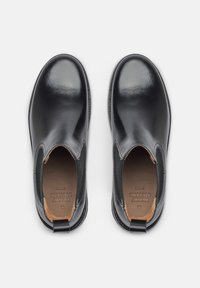 Stivaletti neri in pelle con finitura liscia, pannelli laterali elasticizzati e un inserto a contrasto in pelle marrone sul tallone. Gli interni presentano un marchio impresso.