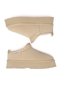 Beige Slippers aus weichem Material. Sie verfügen über ein strukturiertes Obermaterial, genähte Nähte und eine dicke, gerillte Gummisohle.