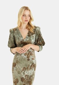 Samtgrünes Kleid mit tiefem V-Ausschnitt, Puffärmeln und floralem Muster in Braun und Bronze. Glatte Textur und taillierte Silhouette.