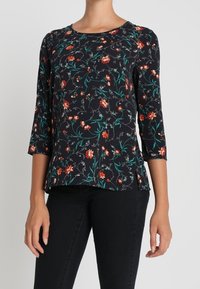 Schwarze Blumenbluse mit drei Viertelärmeln, die rot-grüne Blumenmuster auf dunklem Hintergrund zeigt, aus leichtem Gewebe gefertigt.