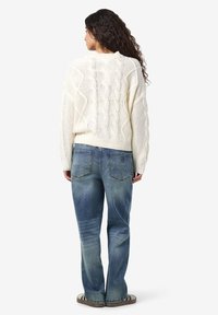 Grietos spalvos megztinis su kabelių raštu ir laisvu siluetu, derinamas su išblukusiais mėlynais džinsais. Megztinis pasižymi tekstūrišku dizainu; džinsai turi galines kišenes.