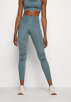 Leggings de sport en teal avec taille haute, en tissu extensible, et détails de couture sur les côtés ; associés à un soutien-gorge de sport assorti et des baskets.