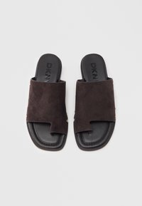 Ζευγάρι μαύρες παντόφλες χωρίς λουριά με σουέντ επάνω μέρος και λουράκι δακτύλου, με το λογότυπο DKNY στο μαξιλαρωμένο πέλμα, παρουσιάζονται σε λευκό φόντο.