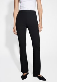 Schwarze Schlaghosen aus glattem Stoff, mit einem elastischen Bund und einem schlichten Design. Kombiniert mit schwarzen spitzen Ballerinas für einen Kontrast.