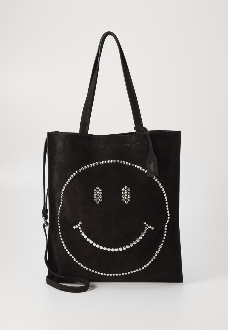 Geantă tote din suede negru cu un design de față zâmbitoare cu ținte argintii și două curele de umăr, pe un fundal simplu.