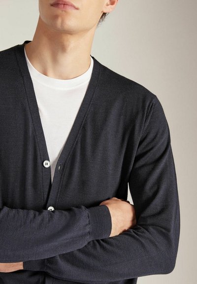 Cardigan noir marine avec un col en V, un front à boutons et des poignets côtelés. Porté par-dessus un T-shirt blanc, mettant en valeur un tissu doux et léger.