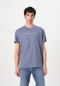 Szürke pamut póló rövid ujjakkal és kerek nyakkal, elöl "TOMMY JEANS" felirattal és logóval. Klasszikus szabás, sima textúra.