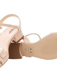 Sandali in pelle sintetica beige con sottili cinturini e tacco basso a blocco. Suola testurizzata con dettagli del marchio e della taglia stampati all'interno.