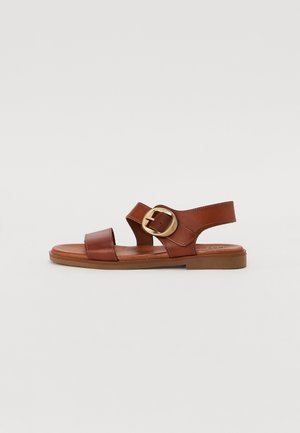 Brown leather sandal with two wide straps and a round gold buckle. Flat sole with a smooth texture. Open-toe design.