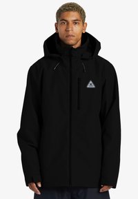 Chaqueta negra impermeable con capucha, que cuenta con una cremallera frontal, un bolsillo en el pecho y un acento de logotipo triangular. Textura suave; corte holgado.