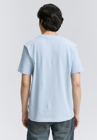 Tricou albastru deschis cu maneci scurte, guler rotund, textură netedă și croială lejeră, asortat cu blugi de denim închis, având buzunare din spate curbate.