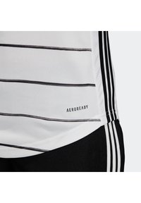 Maglia sportiva bianca con sottili righe orizzontali nere e righe verticali laterali nere, etichettata "AEROREADY", abbinata a pantaloni corti neri con strisce bianche.