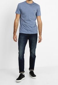 Blue cotton crew neck t-shirt with short sleeves and small logo, paired with dark denim jeans and black sneakers. Casual fit.
