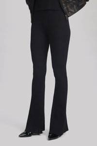 Des pantalons évasés à côtes noirs présentent un tissage texturé et une finition fendue. Portés avec des talons aiguilles noirs, créant une silhouette élancée.