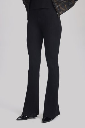 Black ribbed flared pants feature a textured weave and a split hem. Worn with pointed black heels, creating a streamlined silhouette.