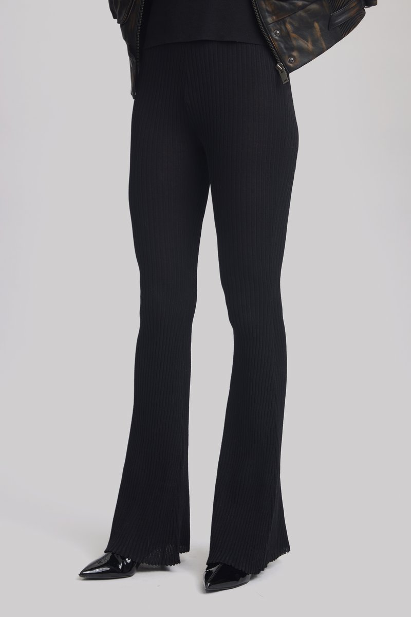 Des pantalons évasés à côtes noirs présentent un tissage texturé et une finition fendue. Portés avec des talons aiguilles noirs, créant une silhouette élancée.