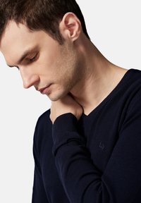 Granatowy, dziany sweter typu V-neck z teksturowanym wzorem i ściągaczami przy mankietach. Subtelne logo na klatce piersiowej. Gładka tekstura materiału.