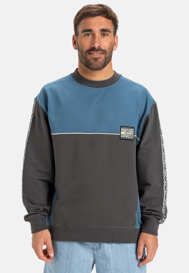 Felpa color-block con pannelli blu e grigio scuro, polsini a coste e rifiniture decorative sui lati con un logo sul petto.