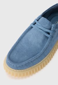 Blue suede shoe with a rounded toe, rubber sole, and textured detailing. Features matching laces and a soft fabric interior.