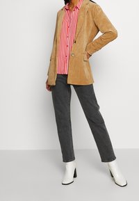 Corduroy tan blazer over a red and white striped shirt, paired with dark gray jeans and white heeled ankle boots.
