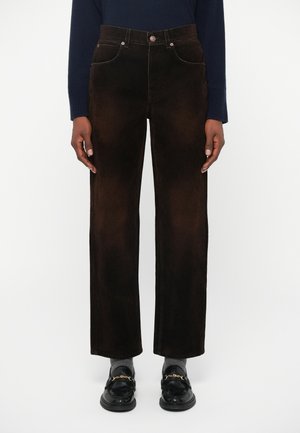 Rjave kordurojske hlače z visokim pasom, ravno krojeno, s vidnimi šivi in sprednjimi žepi. Dopolnjene z črnimi loaferji.