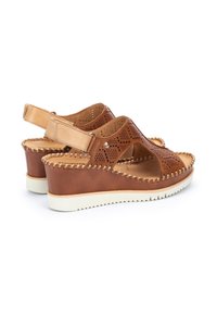 Sandales compensées en cuir marron avec un design perforé, une sangle arrière réglable et une semelle en caoutchouc blanc. Présente un accent tissé le long du bord.