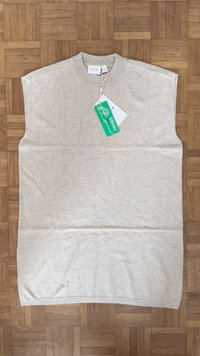 Bež brezrokavni pleten top, narejen iz mehkih materialov. Ima visok ovratnik, subtilen rebrast rob in priloženo oznako.