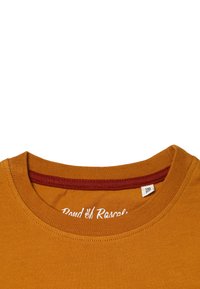 Senfgelbes T-Shirt mit Rundhalsausschnitt, ausgestattet mit einem bordeauxfarbenen Innenkragen und einem weißen Drucktextetikett am Hals. Glatte Textur.