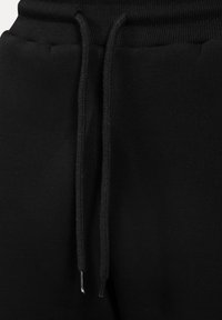Pantalon de survêtement noir avec une taille à cordon de serrage à détails tressés et embouts métalliques, confectionné dans un tissu doux et lisse à texture mate.