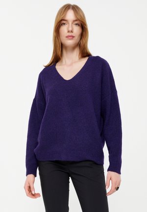 Lila V-Ausschnitt-Pullover mit einem lässigen Design, aus strukturiertem Stoff gefertigt. Mit überschnittenen Schultern und gerippten Bündchen, kombiniert mit schwarzen Hosen.