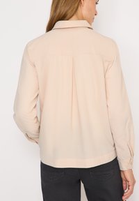 Camicia beige chiaro con colletto, dettaglio di piega sul retro, maniche lunghe e polsini con bottoni. Tessuto liscio, design casual.