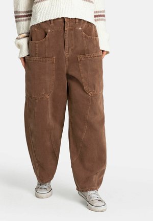 Personne portant un pantalon cargo marron ample avec de grandes poches avant, un pull en tricot blanc à rayures et des baskets blanches.