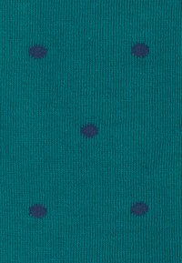 Tissu tricoté teal avec une texture côtelée, présentant des pois navy foncé répartis de manière uniforme.