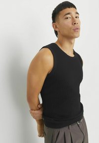 Sort ribbet tanktop med rund hals og ærmeløs design, der har en tætsiddende pasform og struktureret stof, parret med grå plisserede bukser.