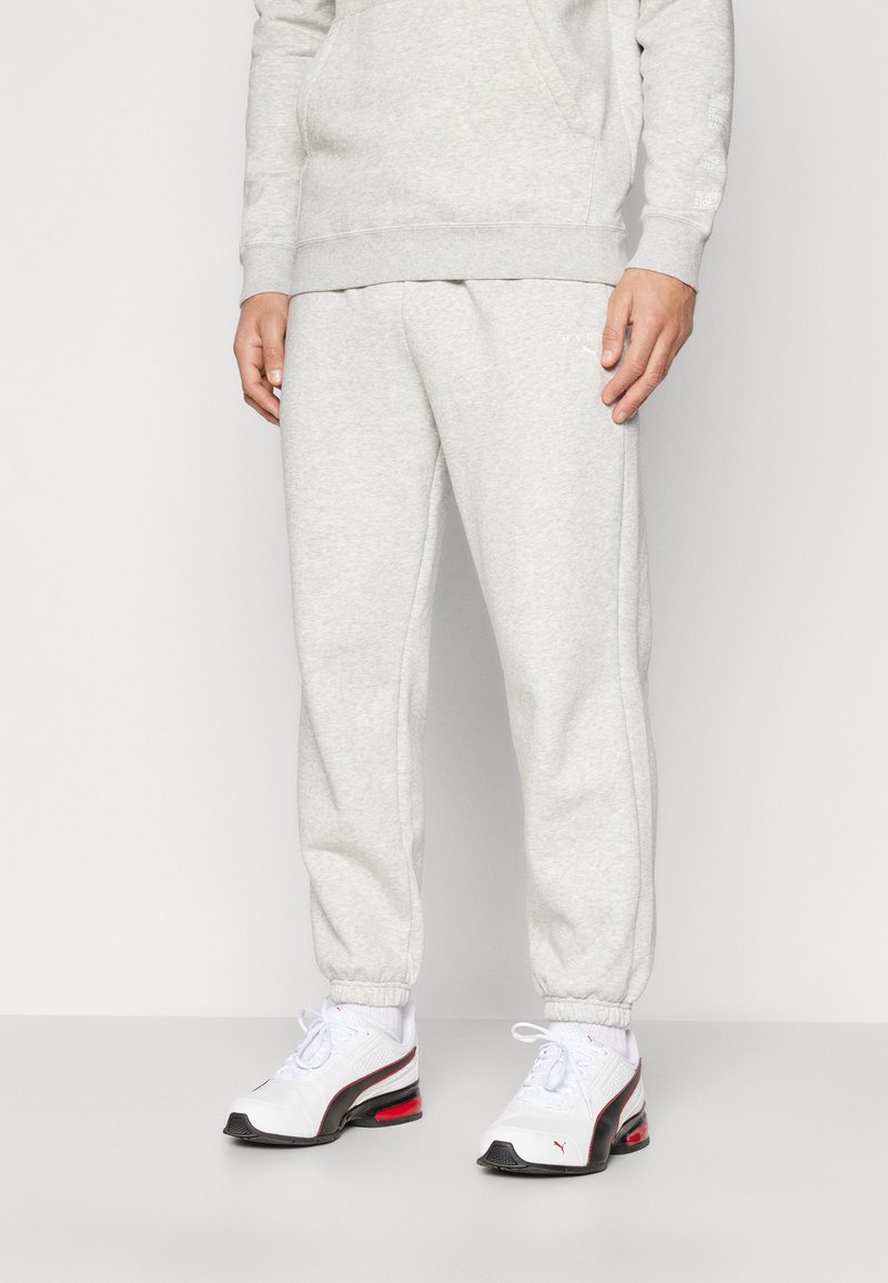 Lys grå sweatpants lavet af en blanding af bomuldsstof, med elastiske manchetter og en justerbar talje, parret med hvide sneakers.