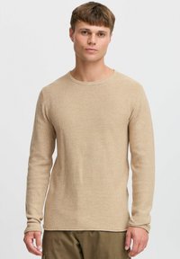 Beiger strukturierter Strickpullover mit Rundhalsausschnitt und langen Ärmeln, der ein dezentes Muster und einen geraden Saum aufweist.