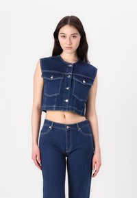 Gilet in denim, cropped e senza maniche, di un blu scuro, con chiusura a bottoni, due tasche sul petto e scollatura rotonda, abbinato a pantaloni in denim.