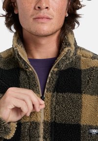 Fleece zip-up jacket in a buffalo check pattern, featuring black and tan colors, with a high collar and visible zipper detail.