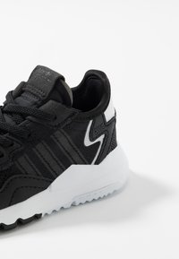 Baskets noires avec une tige texturée, une semelle intermédiaire blanche et des accents contrastants. Conçues avec un système à lacets sur le devant et un col rembourré.