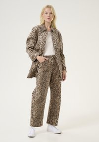 Veste et pantalon imprimés léopard dans des tons beige et marron, présentant un col, une coupe large et des baskets blanches.