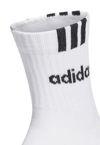 Calcetín atlético blanco con textura acanalada, que presenta franjas negras en la parte superior y el logo de "adidas" en negro en el lateral.