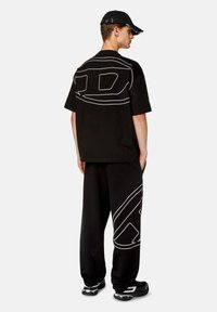 T-shirt oversize nera con design grafico bianco sul retro, abbinata a pantaloni neri con un grafico simile e sneakers nere.