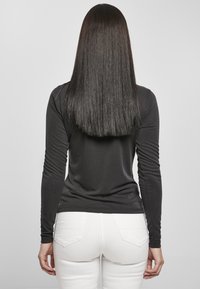 Langermet svart topp med tettsittende design og ribbede detaljer; kombinert med hvite bukser. Glatt tekstur og minimalistisk stil.
