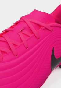 Chaussure de sport rose vif avec des lacets assortis et un logo Nike swoosh noir sur le côté, présentant des rainures texturées et des trous d'aération.